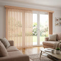 Warm, rich Brown Wood Grain Faux Wood PVC Vertical Blinds filter sunlight while sliding glass doors open onto a serene outdoor patio with wooden deck and lush potted plants.