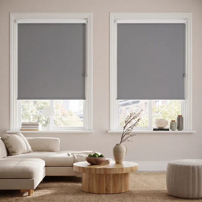 Economy Basic Vinyl Blackout Roller Shades in a modern living room, evoking a cozy atmosphere with gray tones and dimmed light.