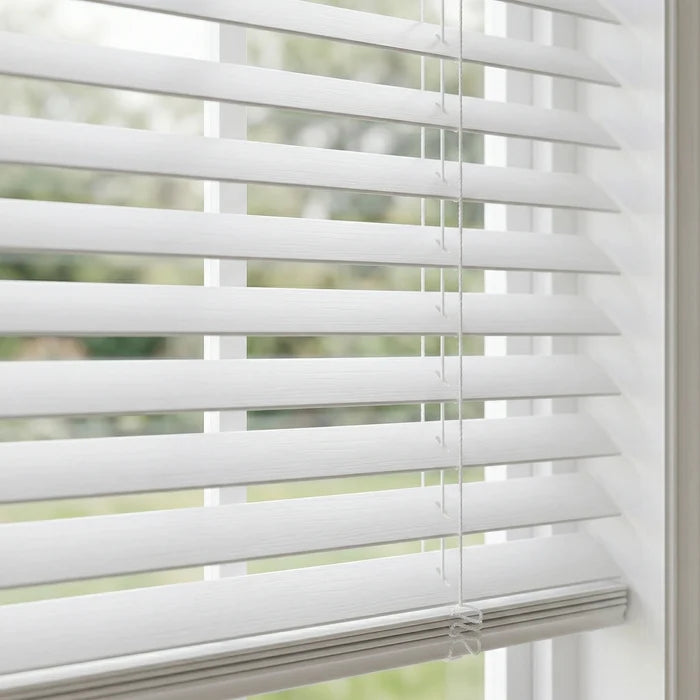 White Venetian blinds partially open with a blurred outdoor background