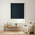 Main view of Marine Black Luxe fabric blackout roller shades in a sun-drenched living room featuring minimalist wooden furniture and neutral decor