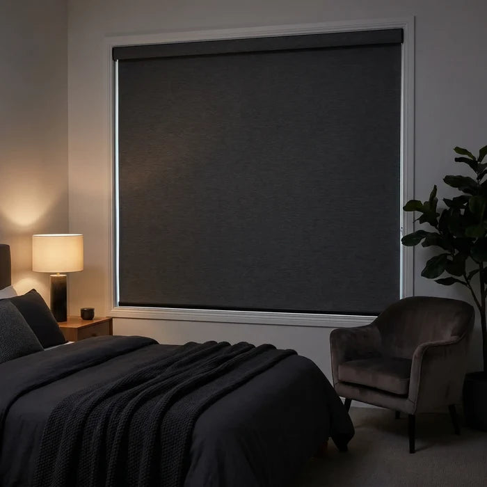 Marine Black Luxe fabric blackout roller shades pulled down in a modern bedroom with a glowing bedside lamp, providing a total dark-sleep environment