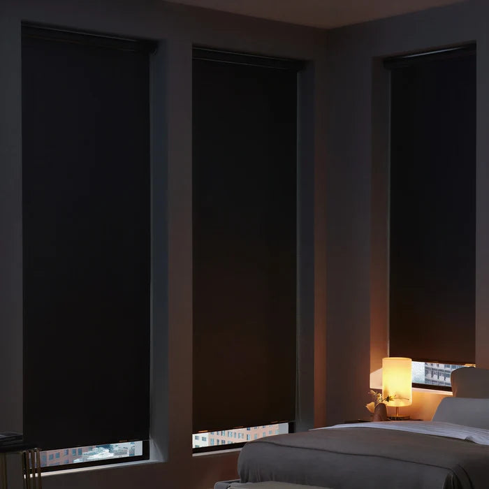 Three black ProGrade blackout roller shades installed on corner windows in a cozy, modern bedroom.