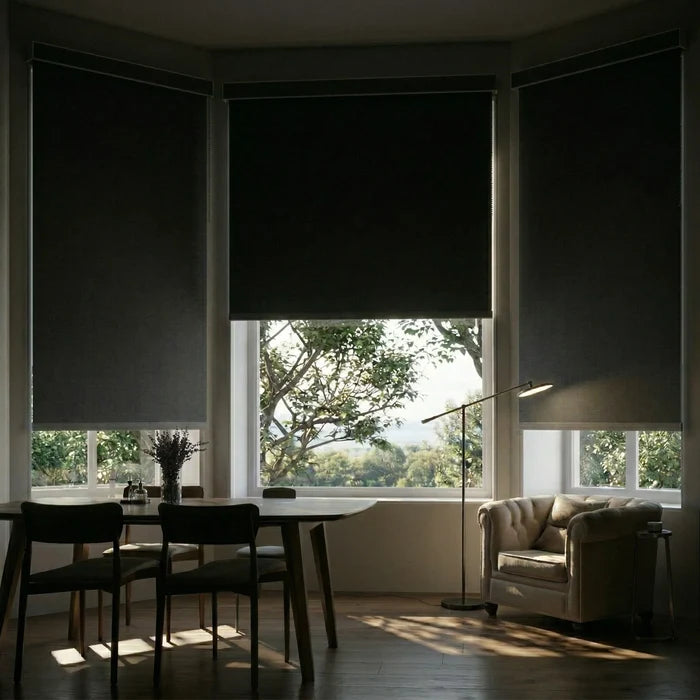 A set of black ProGrade blackout roller shades installed in a bay window dining area to eliminate morning glare.