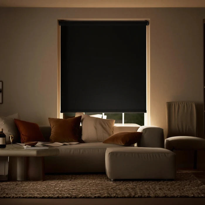 Black ProGrade blackout roller shades in a living room setting, creating a high-contrast look with neutral furniture.
