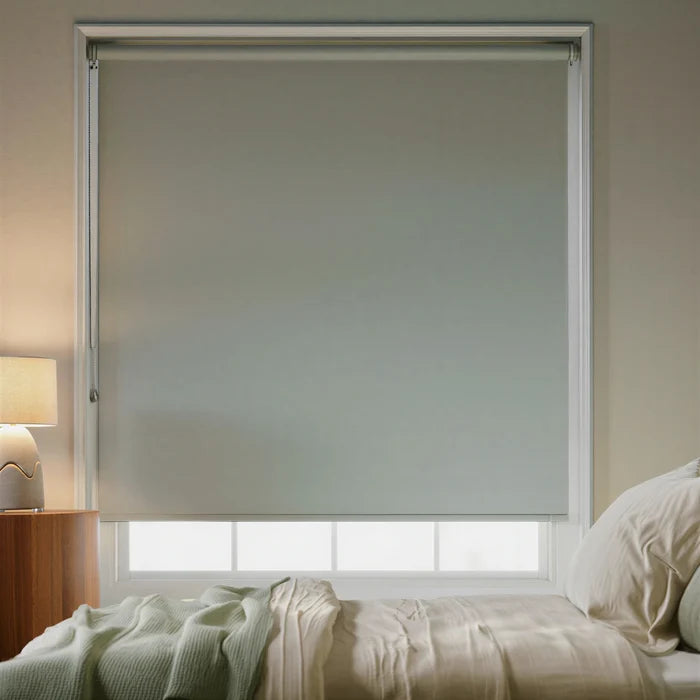 Soft blue-green Light Teal signature blackout roller shades in a guest bedroom with light wood furniture.
