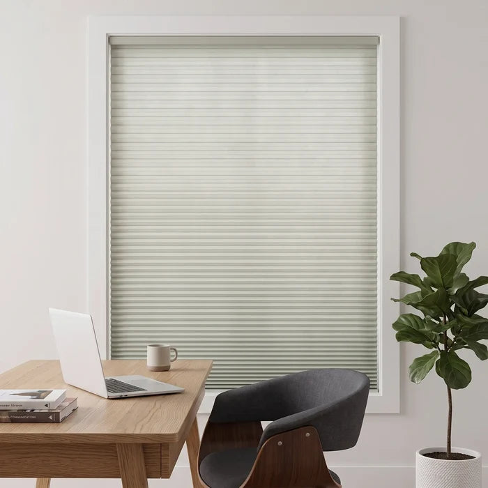 Simplistic Cordless Pleated Shades harmonize with cream-hued walls and wood accents, softly filtering daylight in this serene study featuring a plush armchair and rich leather bookshelf.