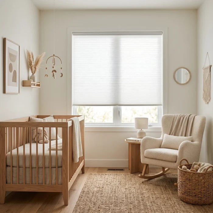 Simplistic Cordless Pleated Shades in Soft White effortlessly complement the nursery's light beige color scheme, allowing gentle sunlight to filter through, while cribs and chairs create a warm haven.